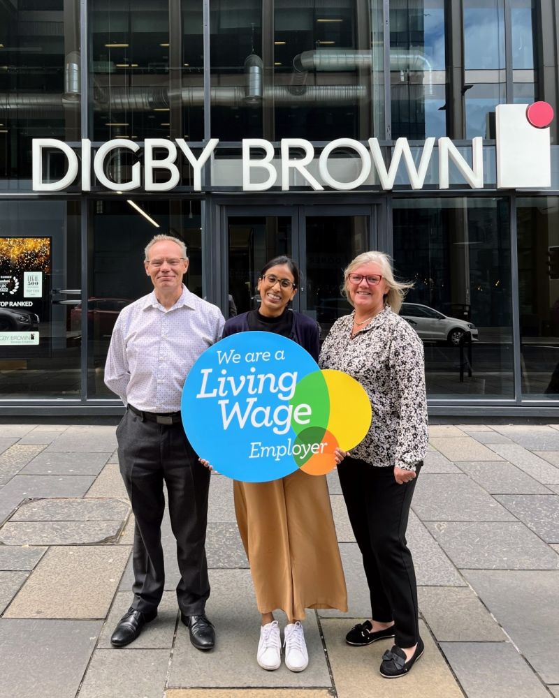 image of degby brown employes infront of building holding card about company and smilling happily